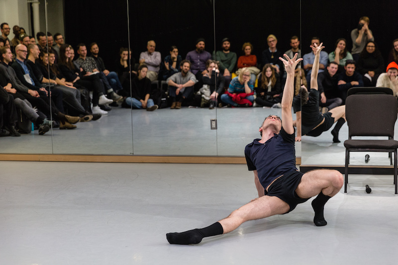 Jack dramatically strikes a pose on the floor. His right leg extends in from of him while he looks up at his hand. 